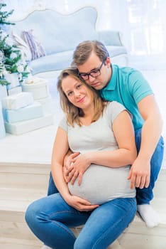 Family portrait near christmas tree. People sitting on the staircase. Pregnant woman