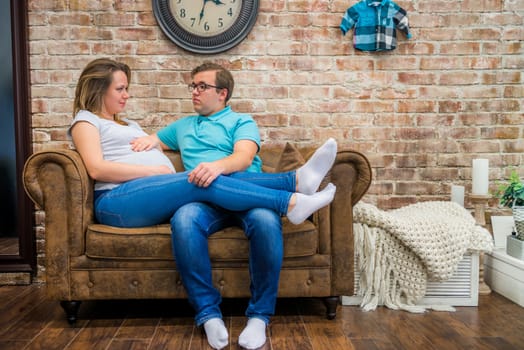 Beautiful pregnant woman and man sitting near brick wall