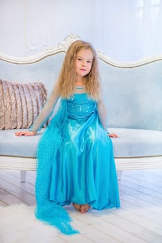 Cute girl in a fancy dress sitting on the sofa.