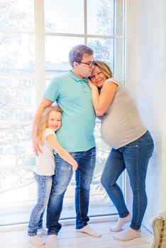 Beautiful pregnant woman, girl and man standing near the window