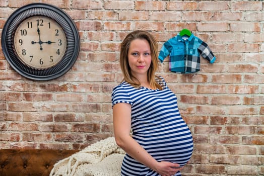 Beautiful pregnant woman sitting near the brick wall.