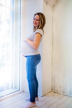 Beautiful pregnant woman standing near window at home.