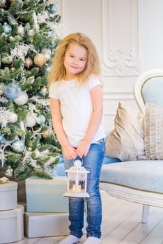 Cute girl in casual clothes and with old lantern on her hands near Christmas Tree