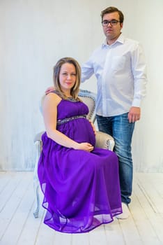 Pregnant woman in an ultraviolet dress with husband sitting on the chair