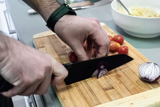 Step by step home cooking salad recepie. Man's hands cutting onions on a wooden board in the kitchen