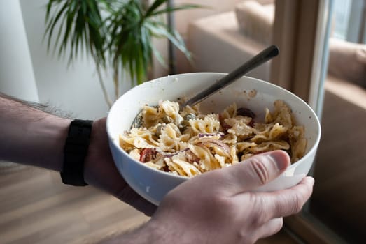 Step by step home cooking salad recepie. Man holds a bowl with ready-made pasta salad at home