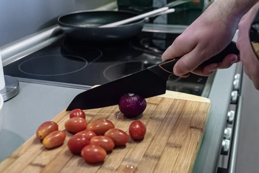 Step by step home cooking salad recepie. Man cuts red onion in kitchen of house against plate