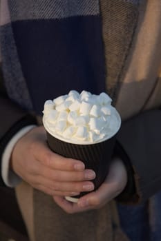 Bright white marshmallows atop cream and a fresh hot chocolate beverage in a disposable takeaway paper cup. Useful for warming hands in winter seasons