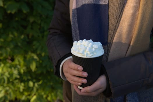Takeaway hot beverage to go, in a disposable yet recyclable black and white paper cup. Green, leafy and outdoors background reflects the environment