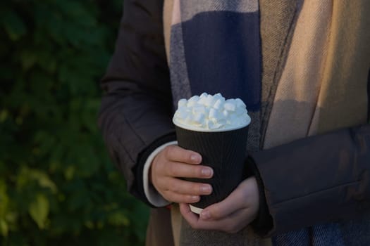 Young girl with a winters coat and woollen scarf holds a fresh takeaway hot chocolate in both hands to keep warm during winter. earthy color tones