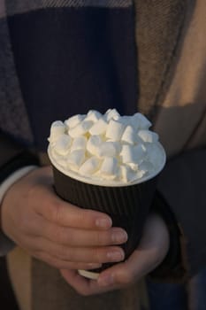 Close up vertical image of a young woman warming her hands on a freshly prepared takeaway hot drink. Winter scarf background, copy space above