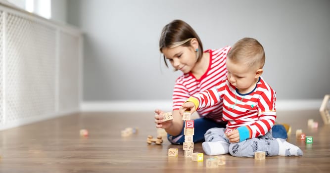 Sister and brother playing with cubes together on the floor indoors. Concept of the family relationship.