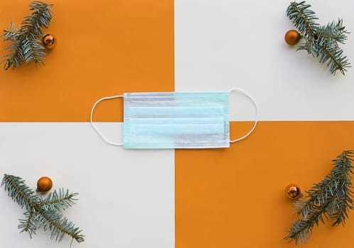 Corona and Christmas. A protective mask next to Christmas tree balls and fir branches on an orange and beige background