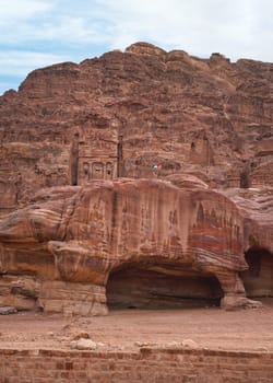 Simple dwelling ruins - cave like holes in stone wall, Jordan flag waves on top, typical Petra scenery.