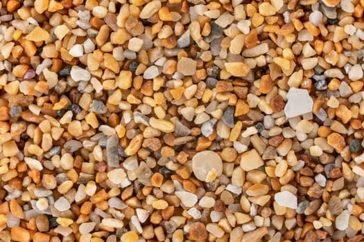 Sea sand Ghajn Tuffieha beach, Malta with reddish orange particles few ocean shell remains visible. Microscope photo, image width 9mm.