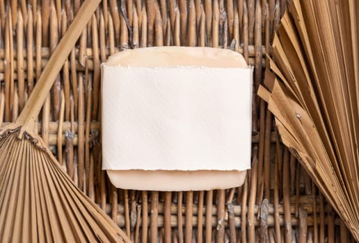 Handmade Soap bar with paper wrapping package and dried palm leaves on a wooden wattled table , top view. Soap mockup tropical or bohemian flat lay, Healthy lifestyle concept