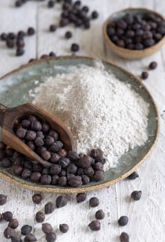 Plate and wooden scoop of black chickpea flour and beans closeup on white wooden table. Traditional beans from Apulia and Basilicata in Italy