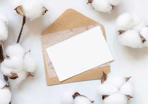 Feminine Wedding card and envelope mockup on white table with cotton flowers top view. Elegant modern template with horizontal blank paper card, flat lay with place for text. Minimalistic stationery scene. Natural, eco-friendly concept