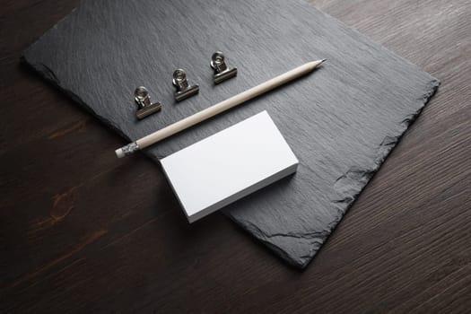 Photo of blank business cards, pencil and metal clamps on stone board background. Template for ID.