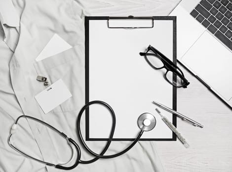 Health care concept. Blank medical clipboard, stethoscope, glasses, badge, thermometer, pen and laptop. Flat lay.