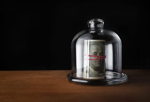 Saving money concept. Dollars under glass cap. Copy space.