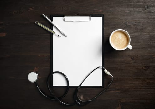 Blank medical clipboard, stethoscope, badge, thermometer, pen and coffee cup on wooden background. Flat lay.