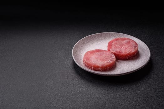 Two fresh slices of raw tuna fillet with spices and herbs on a dark concrete background