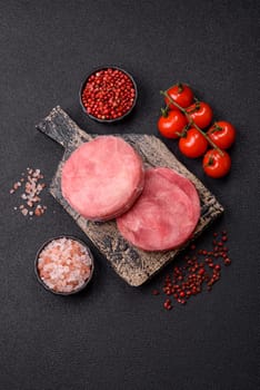 Two fresh slices of raw tuna fillet with spices and herbs on a dark concrete background