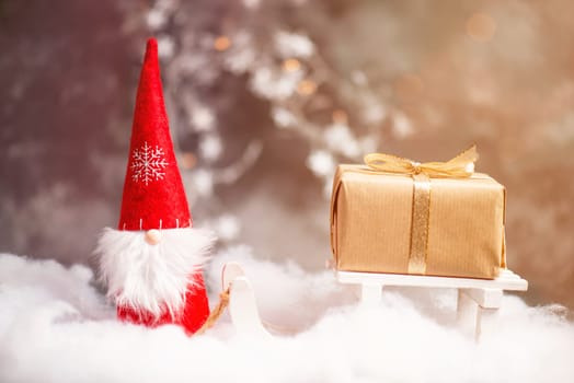 Christmas gnome greeting card with bokeh lights and snow, winter season, gift on the sledge