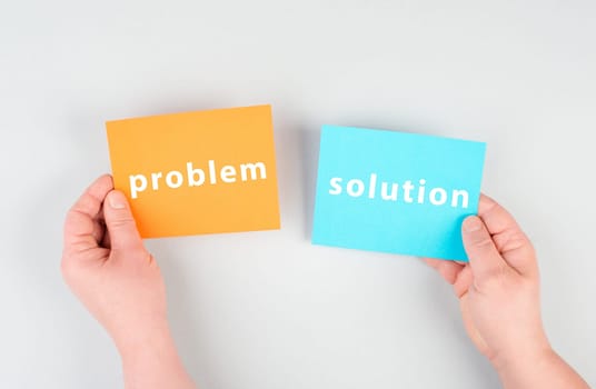 The words problem and solution are standing on orange and blue colored paper, brainstorming for new ideas, hands holding the message