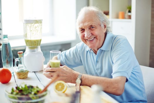 Senior man with glass of fruit smoothie sitting in kitchen