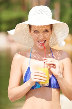 Woman in bikini and hat drinking orange juice outdoors