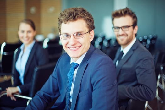 Cheerful manager looking at camera with two colleagues behind
