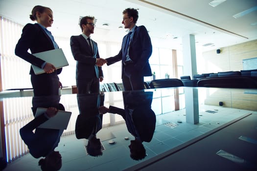 Successful professionals handshaking in office with young businesswoman near by