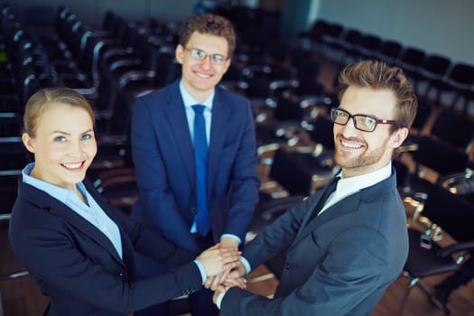 Happy colleagues making pile of hands and looking at camera