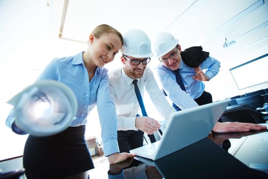 Young architect pointing at laptop display while explaining data to colleagues