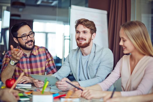 Happy businessman with touchpad and his colleagues communicating in office