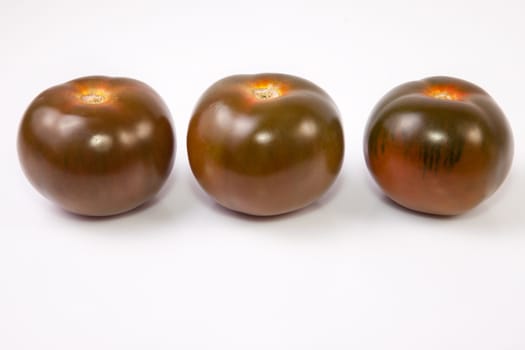 Three dark green kumato tomatoes. Isolated over white background