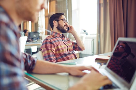 Young businessman sitting by workplace and speaking on the phone
