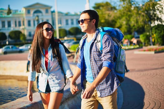 Affectionate travelers with rucksacks enjoying walk in the city