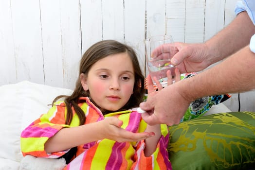 a little girl in bed taking tablet with water
