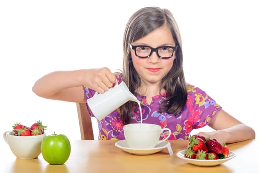 a little girl pours milk into a cup on white
