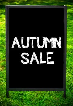 AUTUMN SALE  message on sidewalk blackboard sign against green grass background. Copy Space available. Concept image