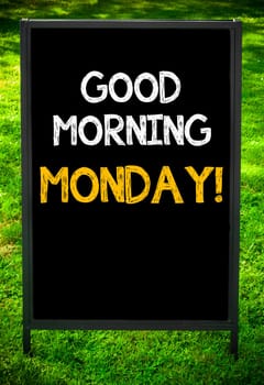 GOOD MORNING MONDAY!  message on sidewalk blackboard sign against green grass background. Copy Space available. Concept image