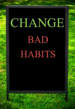 CHANGE BAD HABITS  message on sidewalk blackboard sign against green grass background. Copy Space available. Concept image