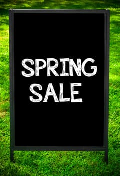 SPRING SALE  message on sidewalk blackboard sign against green grass background. Copy Space available. Concept image