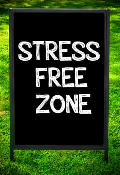 STRESS FREE ZONE  message on sidewalk blackboard sign against green grass background. Copy Space available. Concept image