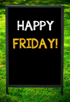 HAPPY FRIDAY message on sidewalk blackboard sign against green grass background. Copy Space available. Concept image