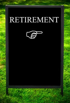 RETIREMENT message and hand pointing to the right on sidewalk blackboard sign against green grass background. Copy Space available. Concept image