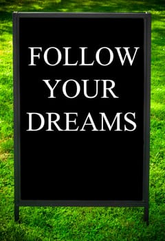 FOLLOW YOUR DREAMS  message on sidewalk blackboard sign against green grass background. Copy Space available. Concept image